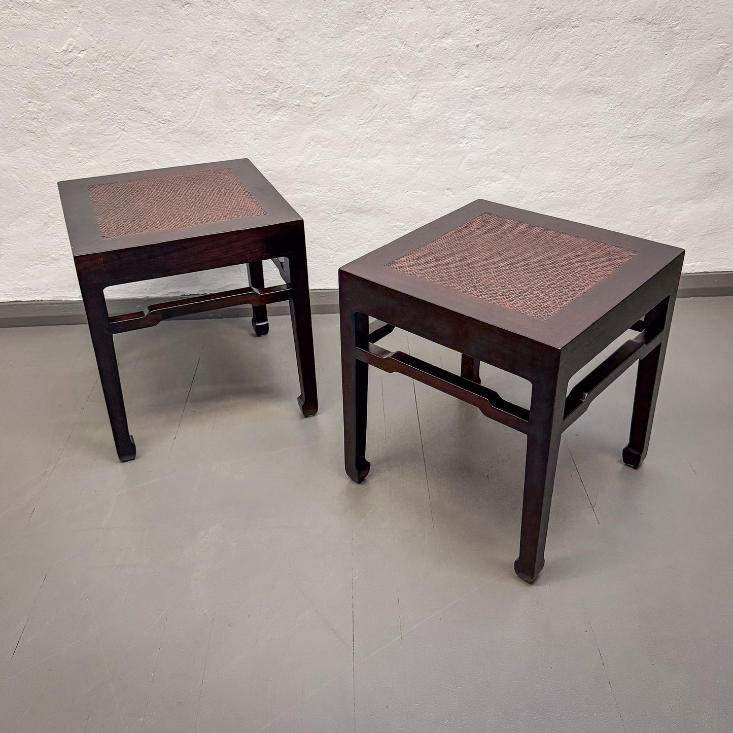 Two dark wooden side tables with woven tops on a plain floor.