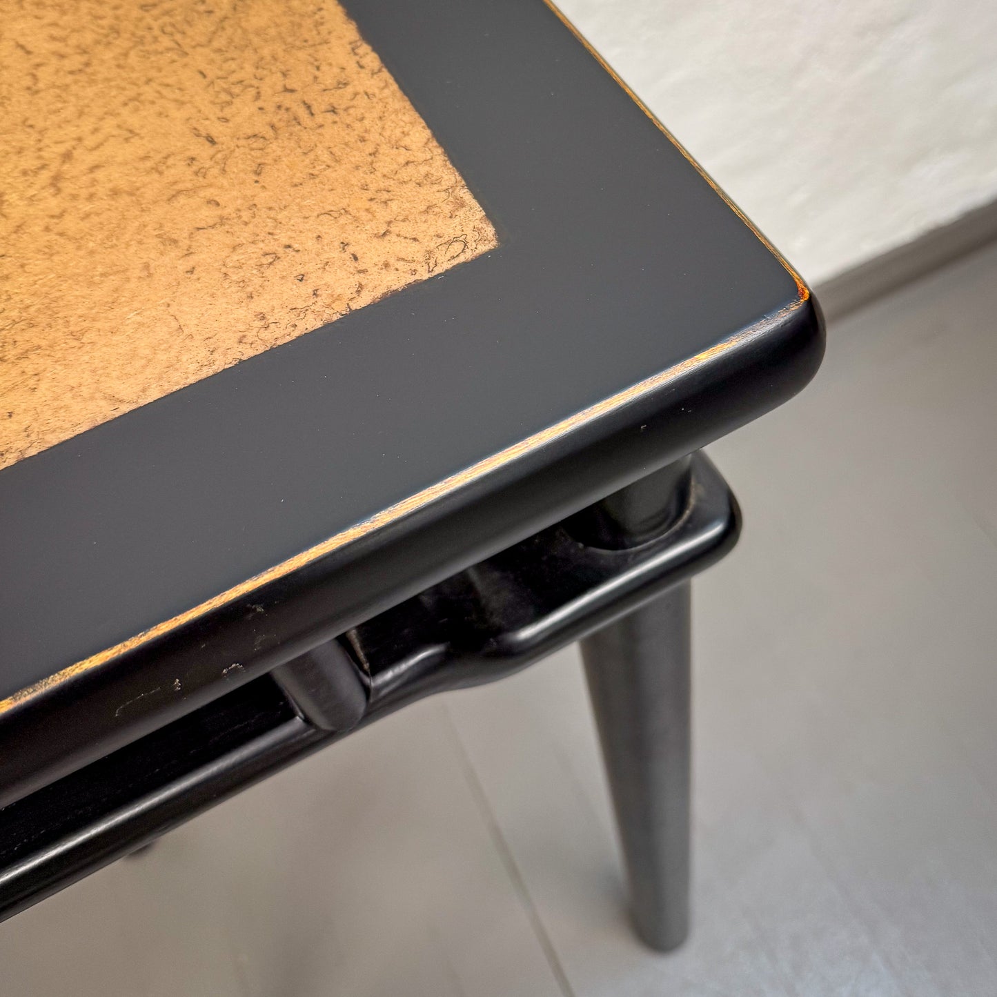 Small table with black frame and cork surface on a white floor.