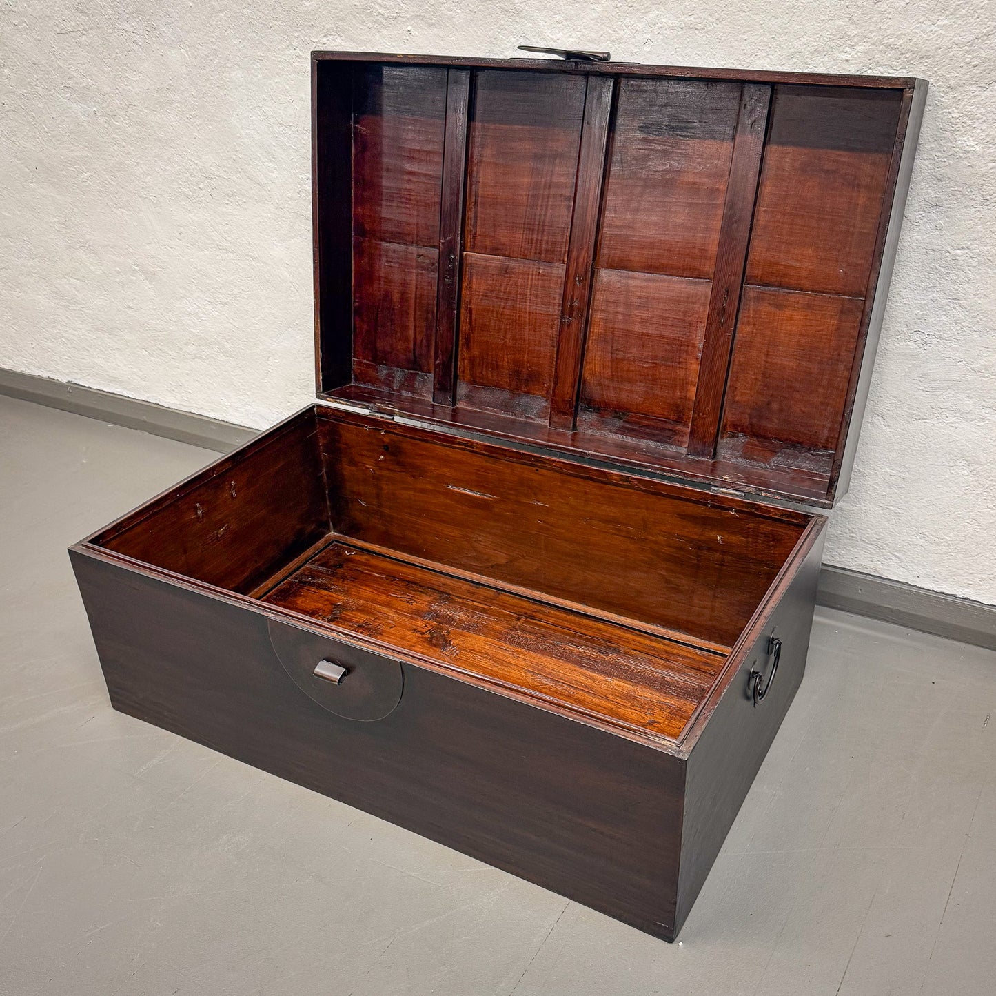 Wooden trunk with a hinged lid on a plain floor.