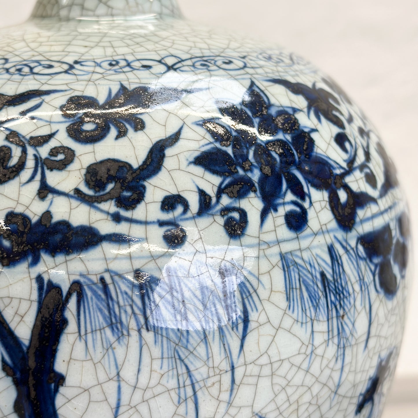 A blue and white porcelain Meiping vase with a floral and country scene design, placed on a flat surface.