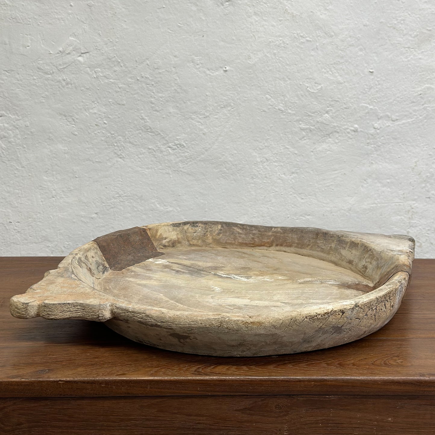 A beige decorative bowl with iron detail, placed on a wooden surface against a plain wall.