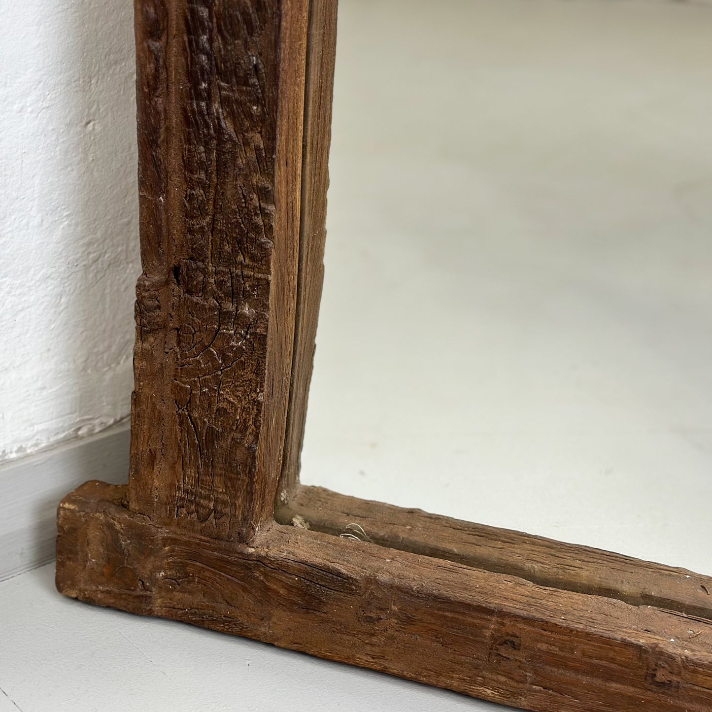 A vintage-style mirror with a carved wooden frame, standing out against a white wall and wooden door backdrop.