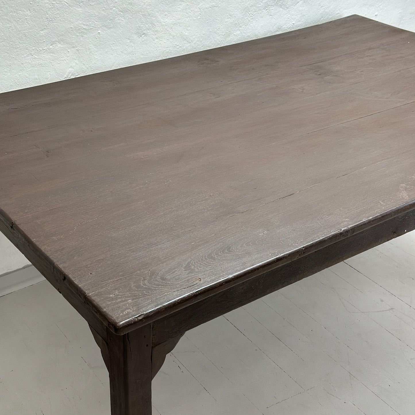 A vintage teak work table with a rectangular top and dark wood legs, placed against a white wall on a white floor.