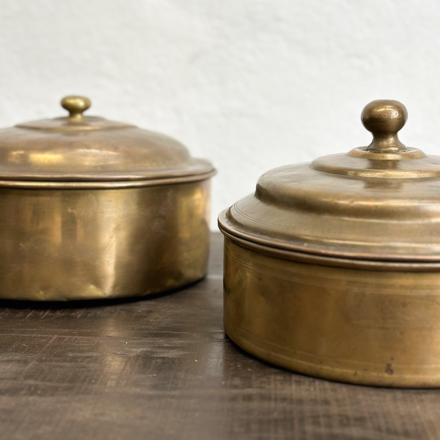 Two brass knob lid chapati boxes with a plain background.
