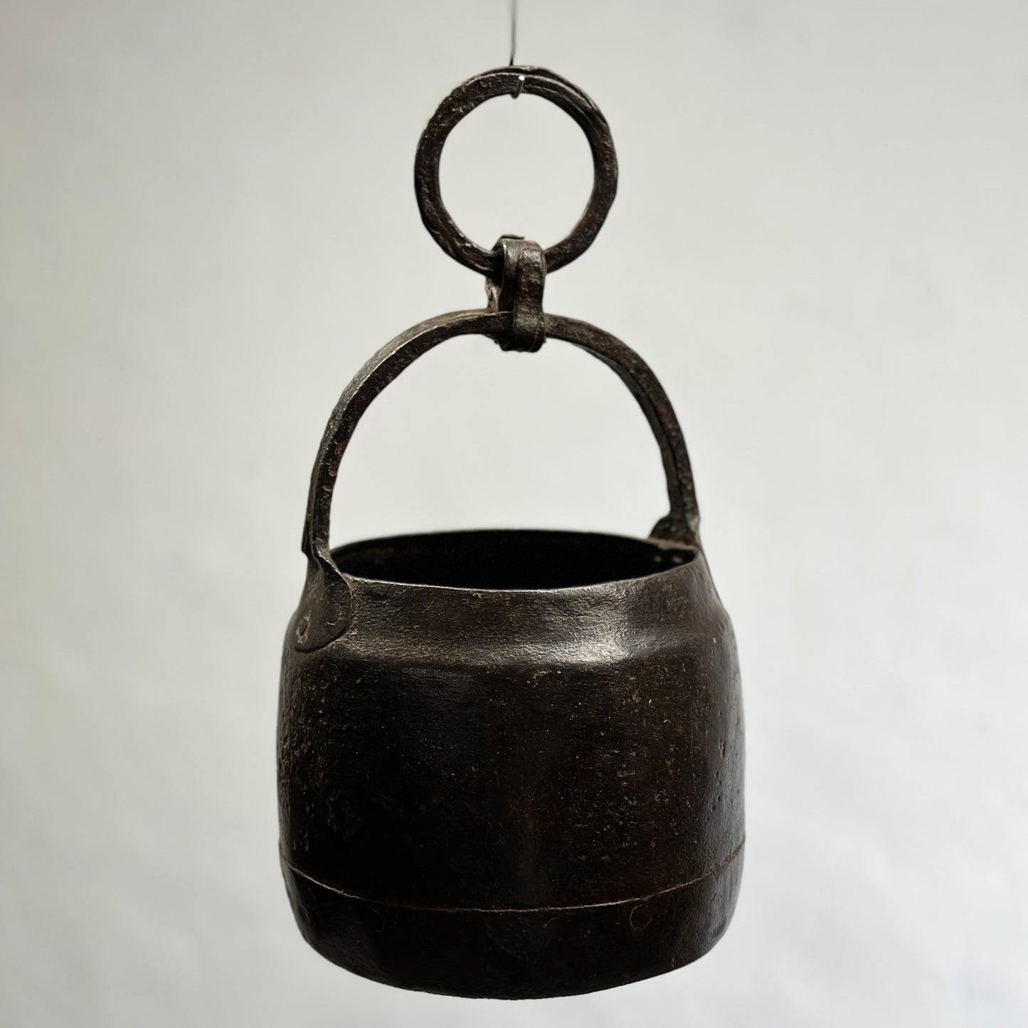 A vintage iron well bucket with a looped handle, hanging against a white background.