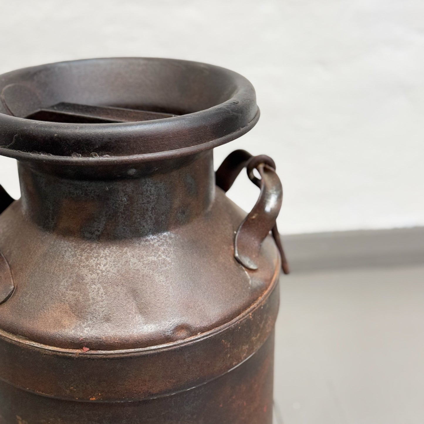 A vintage Indian iron milk storage container with a dark brown patina, featuring two handles on the sides.