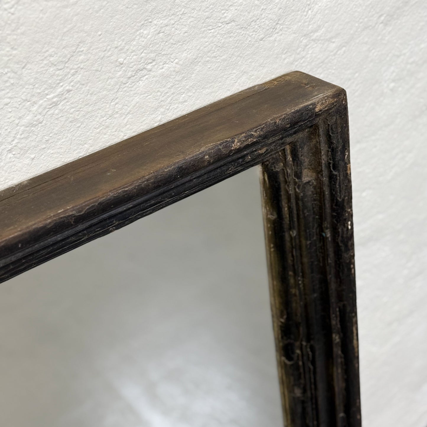 A black vintage teak mirror with a reflective surface, standing against a wall on a floor.