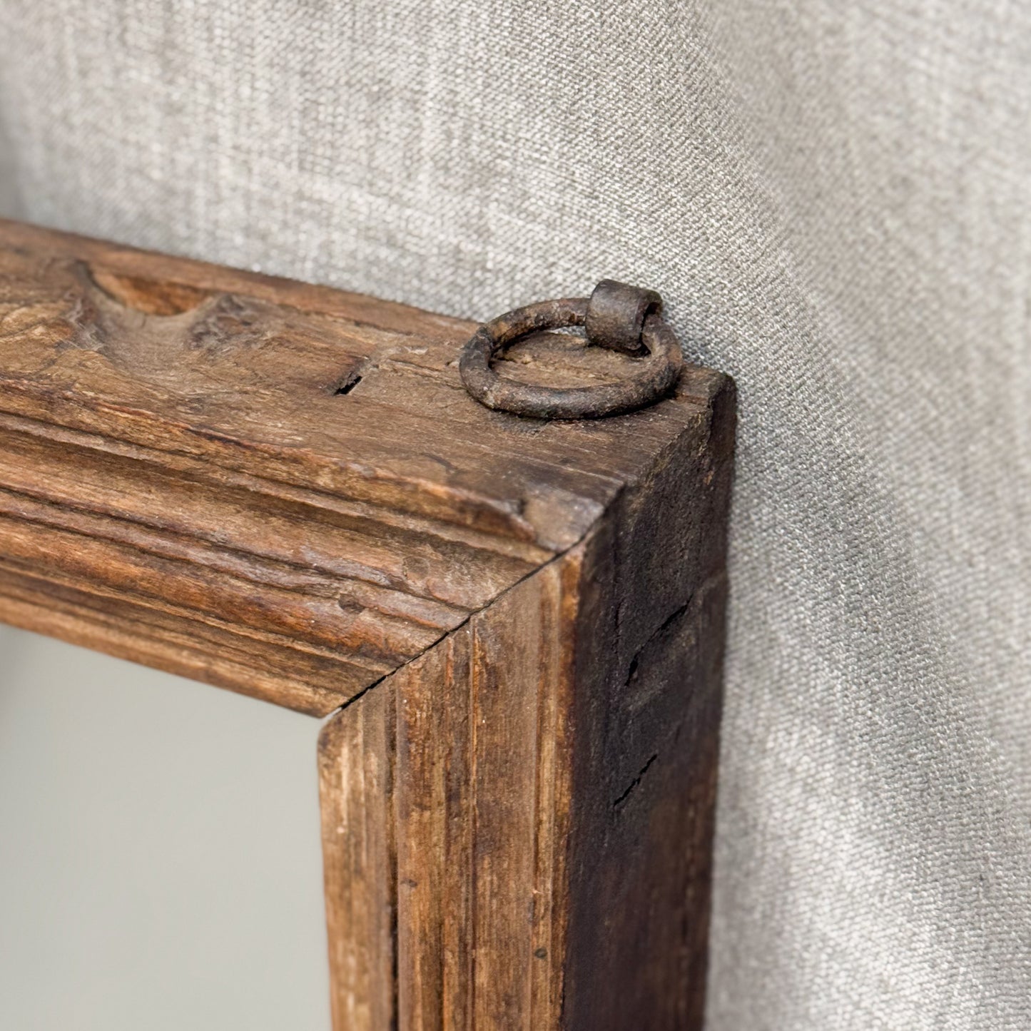 A rectangular large simple vintage teak mirror with a wooden frame, standing against a wall with a draped curtain in the background.