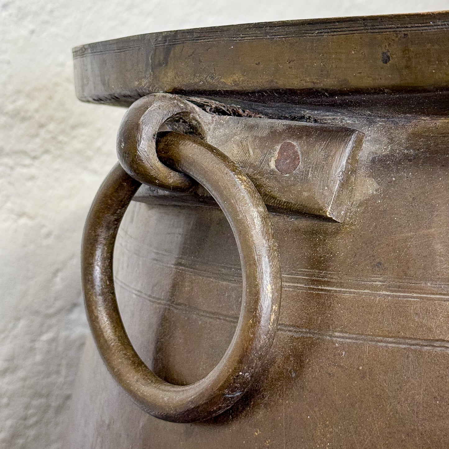Close-up of a bronze pot with a ring handle on a textured white background