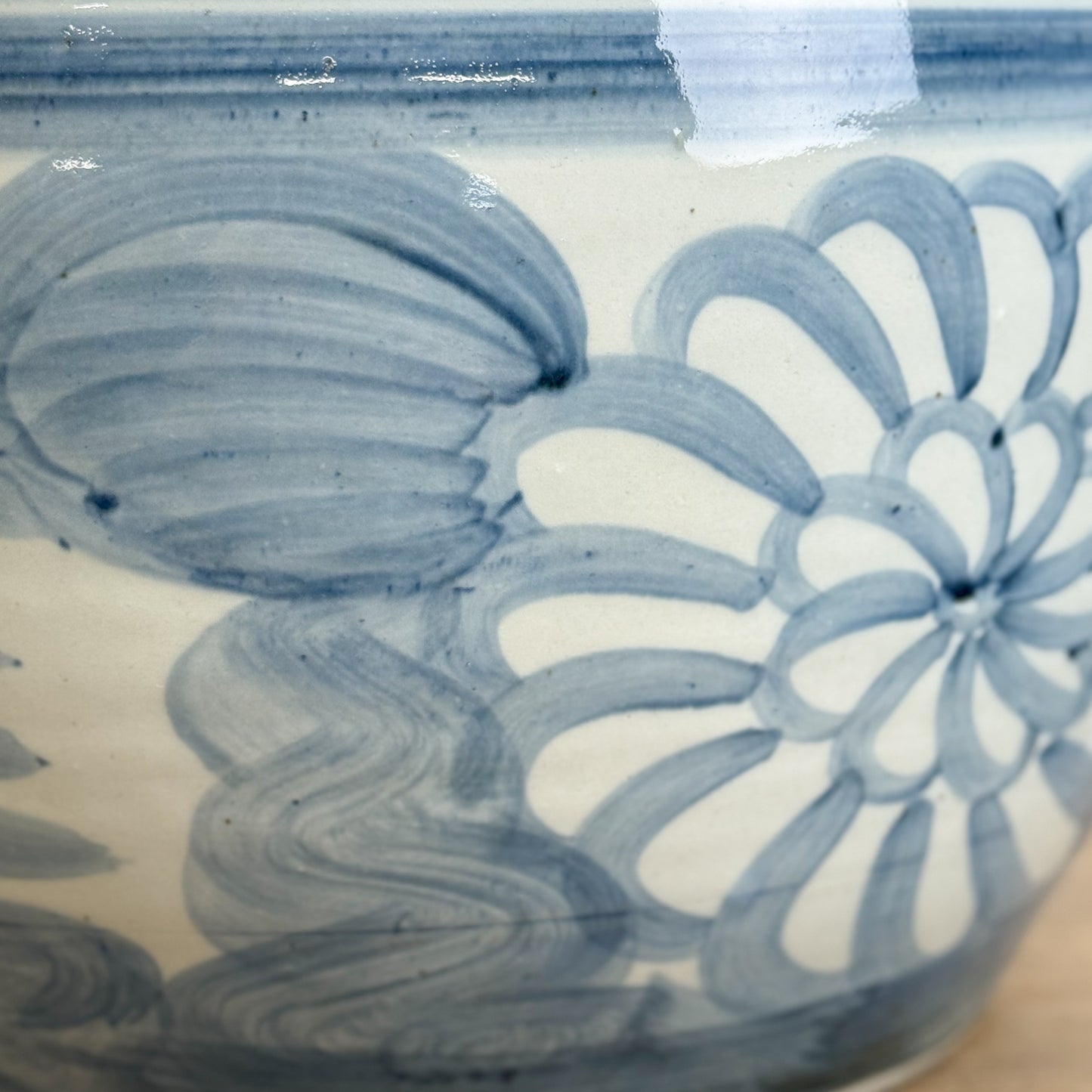 A porcelain planter with cobalt blue floral patterns on a wooden surface against a white wall.