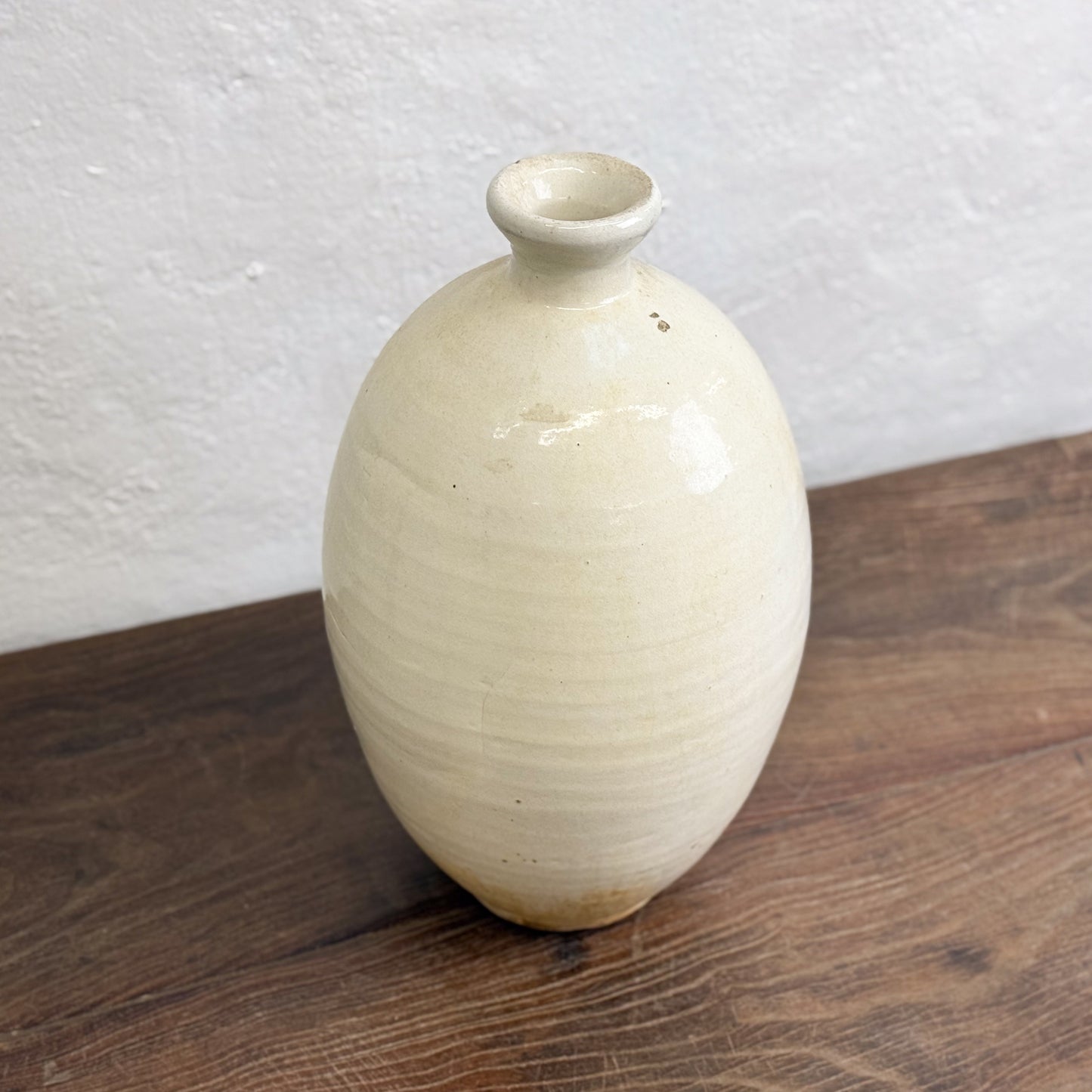 A beige ceramic vase with a simple design, displayed against a neutral background.
