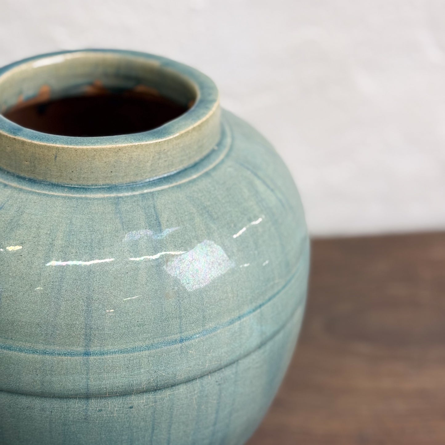 A tall glazed ceramic vase with a greenish tint, displayed against a neutral background.