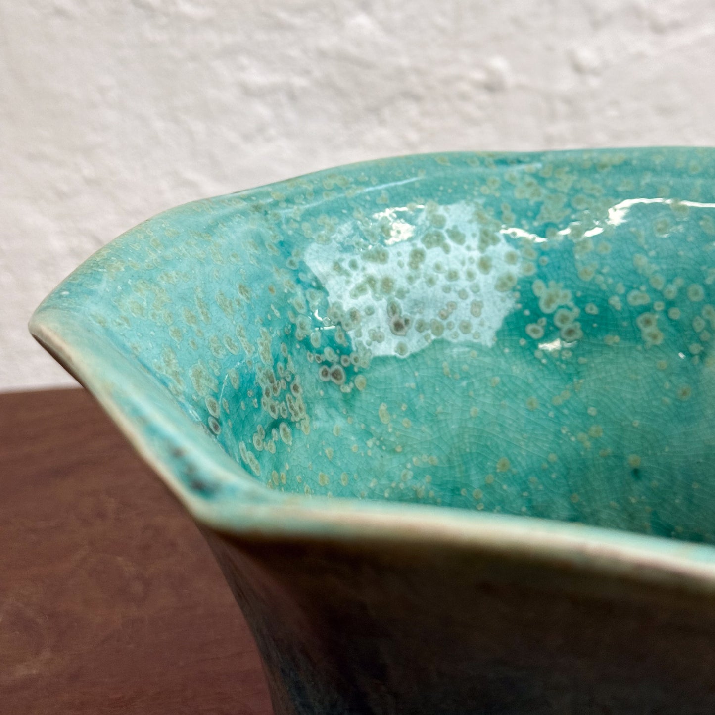 A small, glazed, hexagonal planter with a turquoise color on the upper part and a brown base, placed on a wooden surface against a white background.