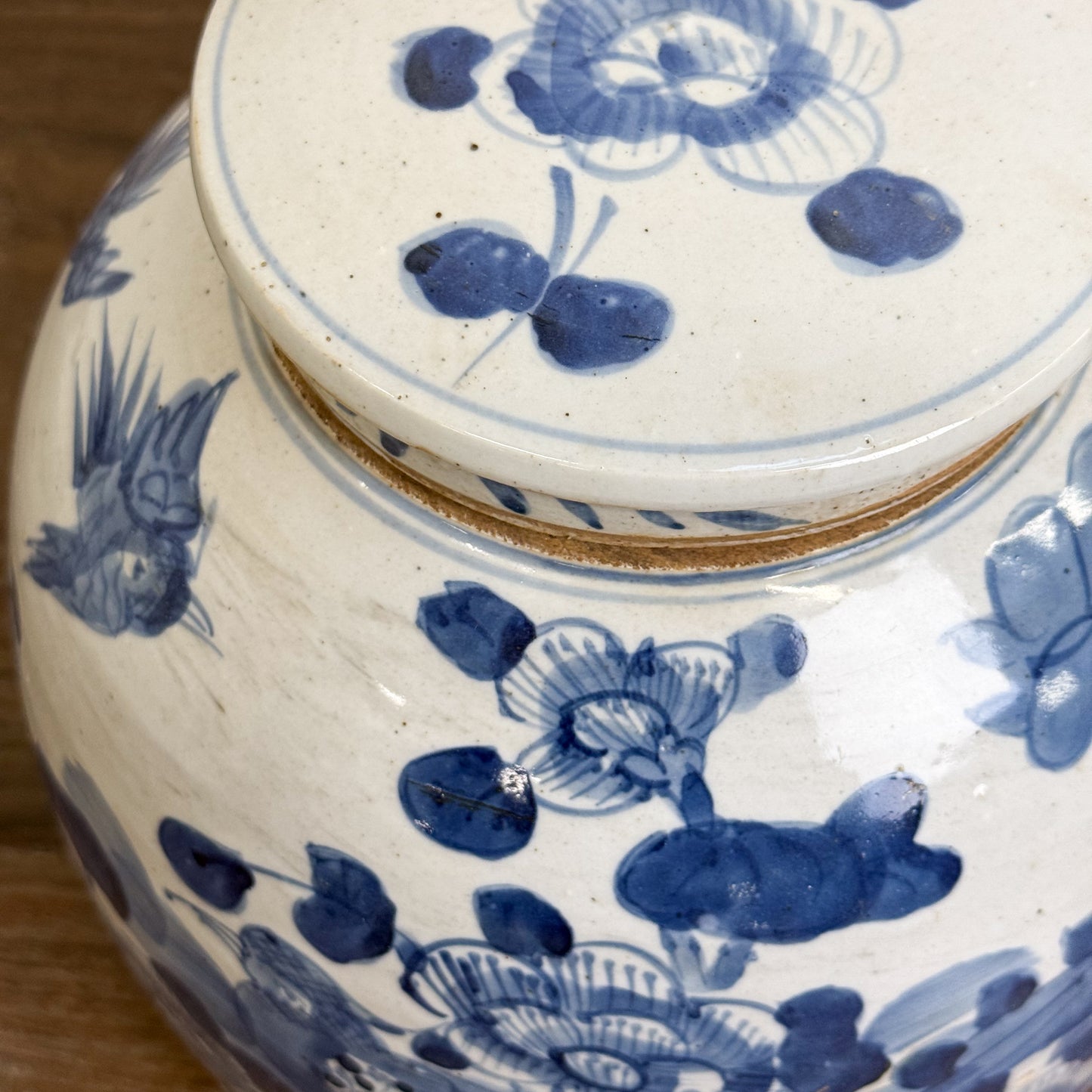 A squat porcelain ginger jar with blue floral patterns on a white background, displayed against a neutral backdrop with a wooden surface.