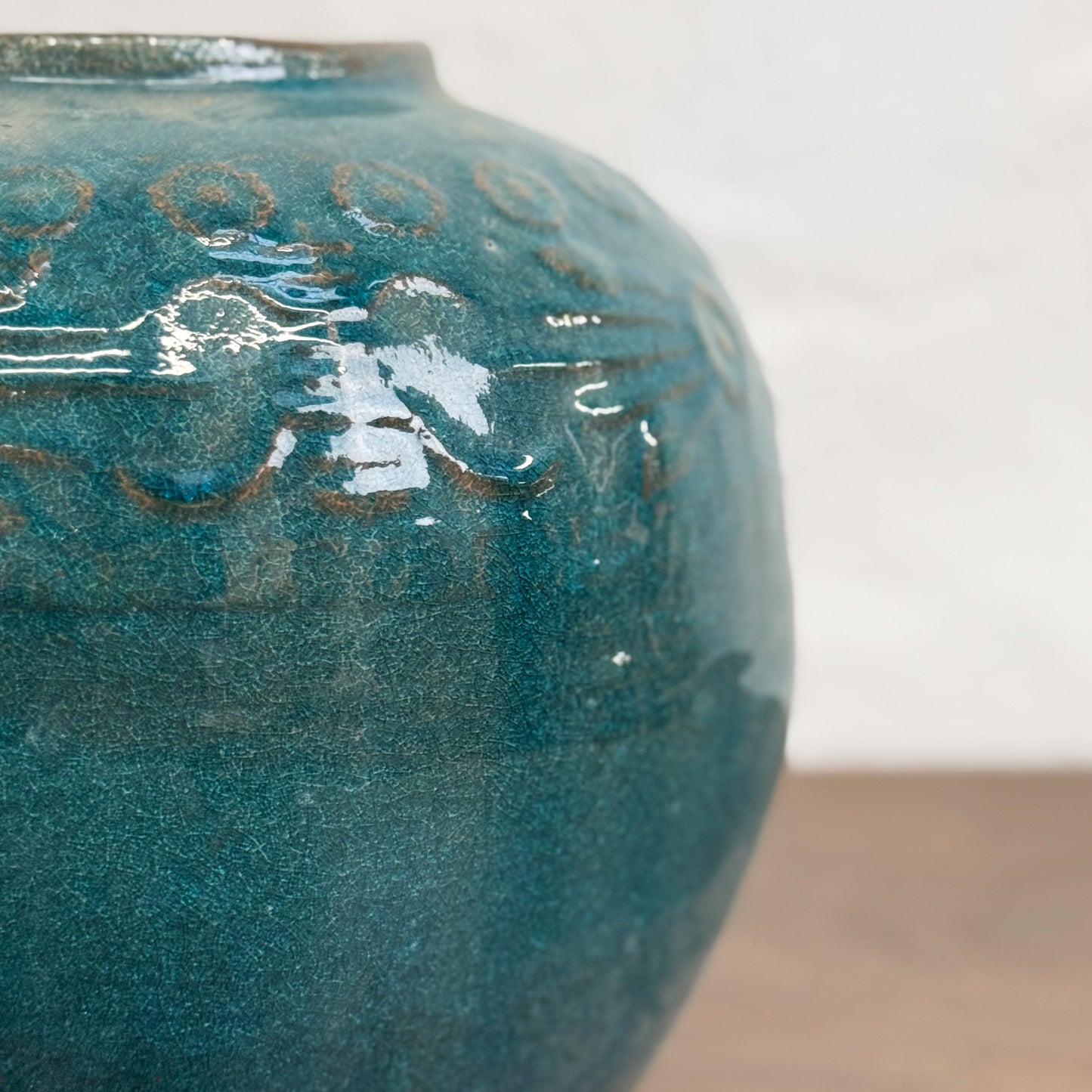 A round embossed ceramic pot with blue and green colors, displayed on a wooden surface.
