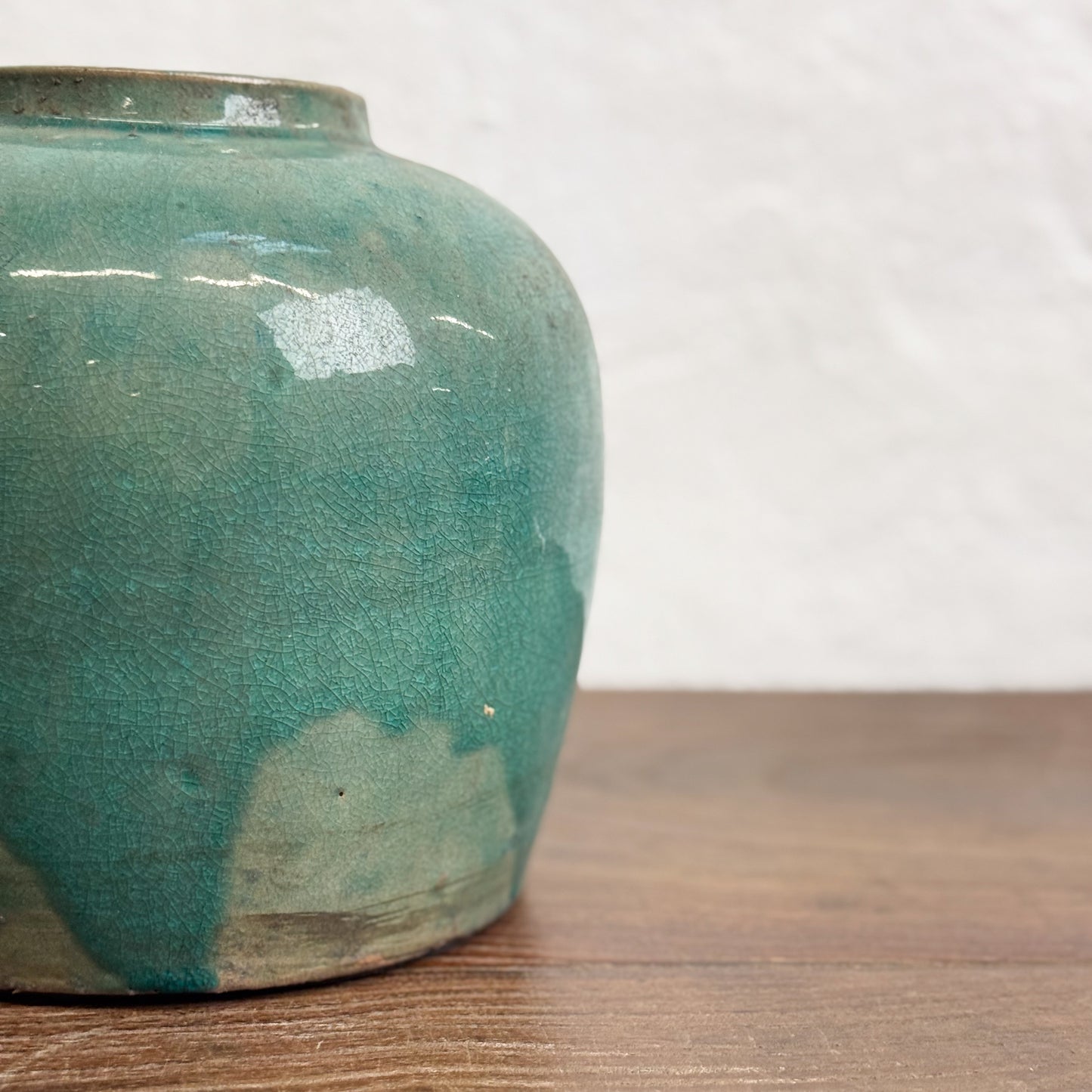 A green glazed ceramic pot with a rounded shape, placed on a wooden surface.