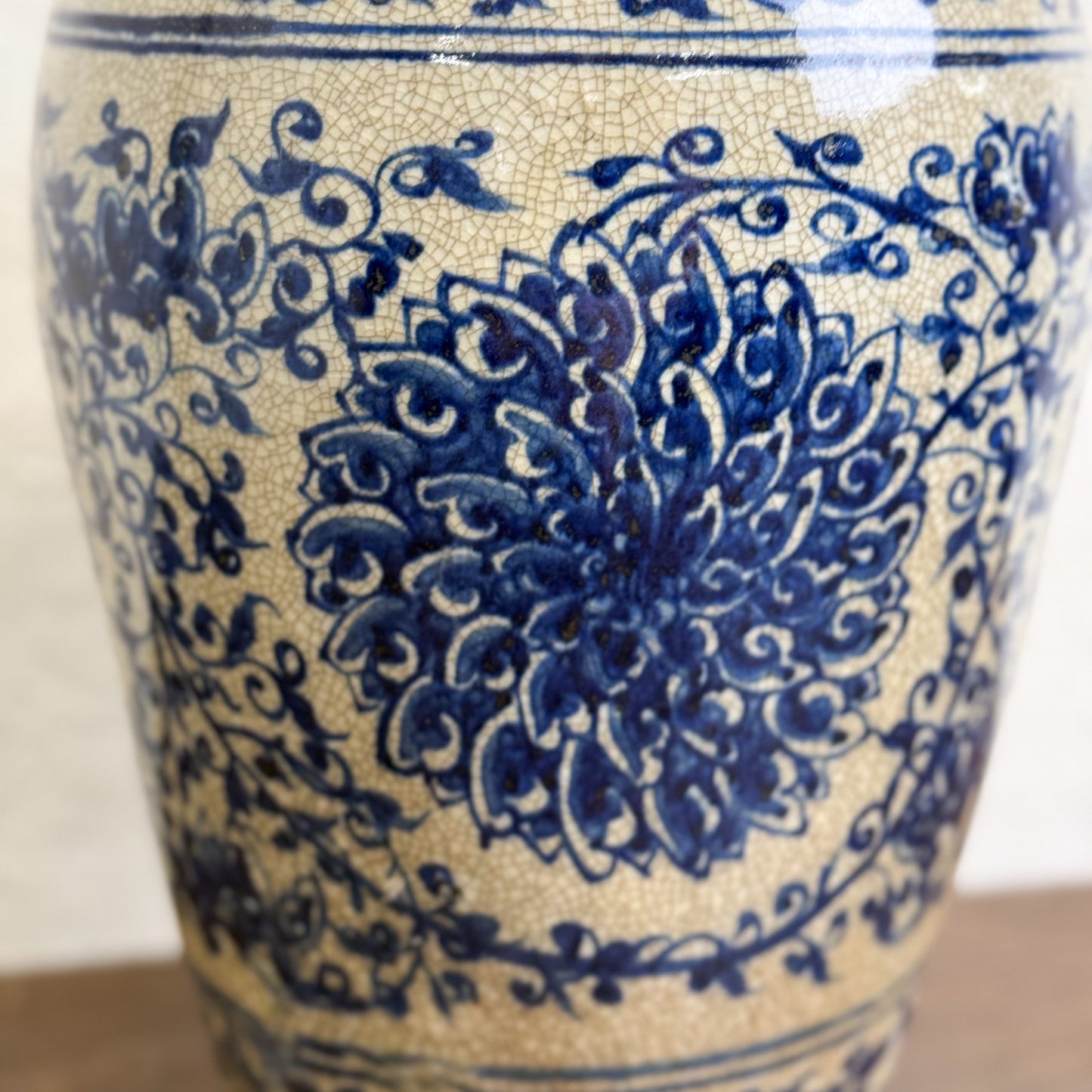 A porcelain vase with blue floral patterns against a white background, placed on a wooden surface.