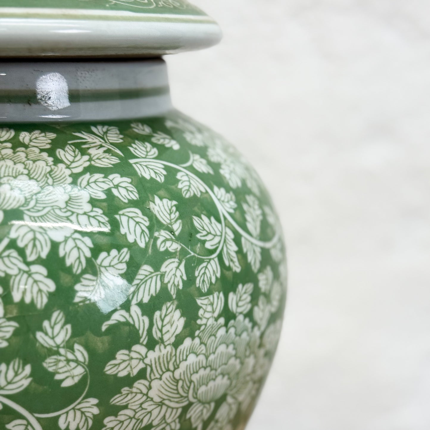 Green ceramic jar with white floral patterns on a white background