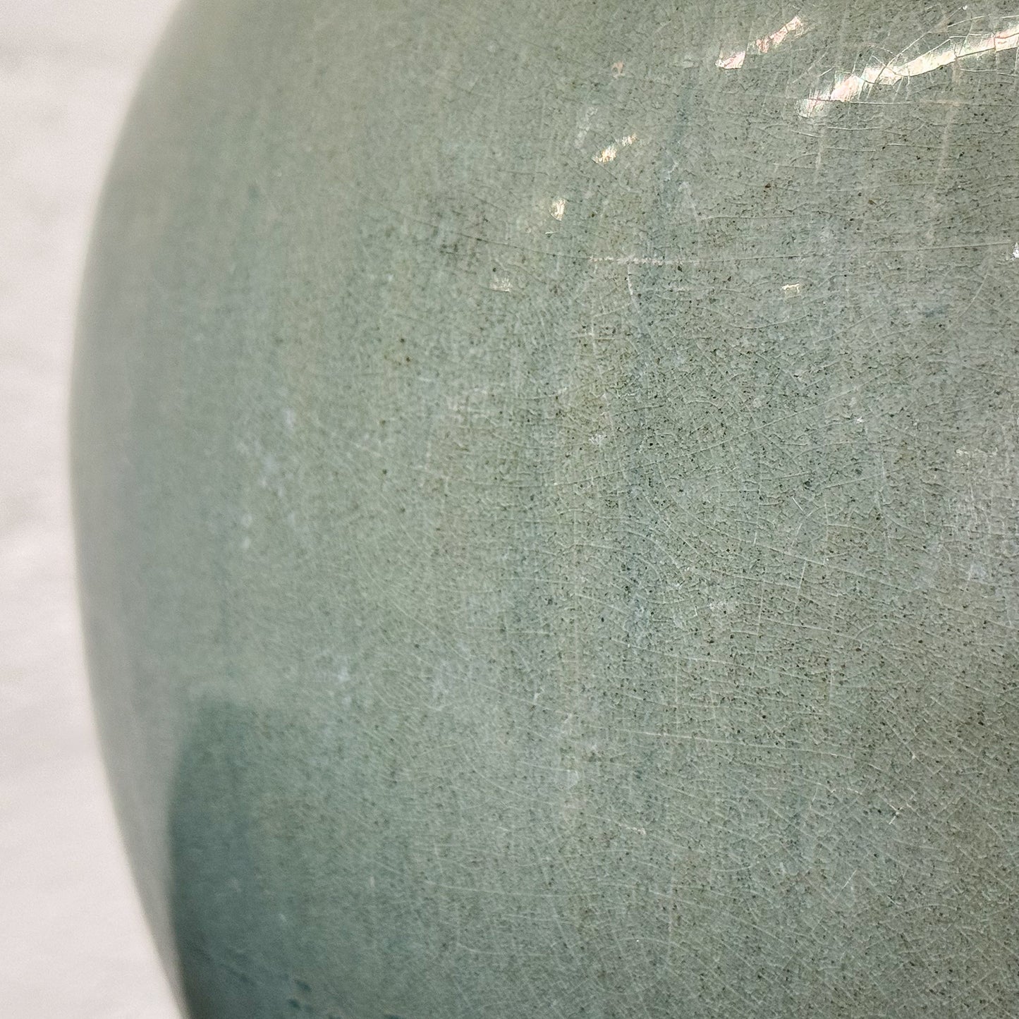 Green ceramic jar on a wooden surface with a white textured wall background