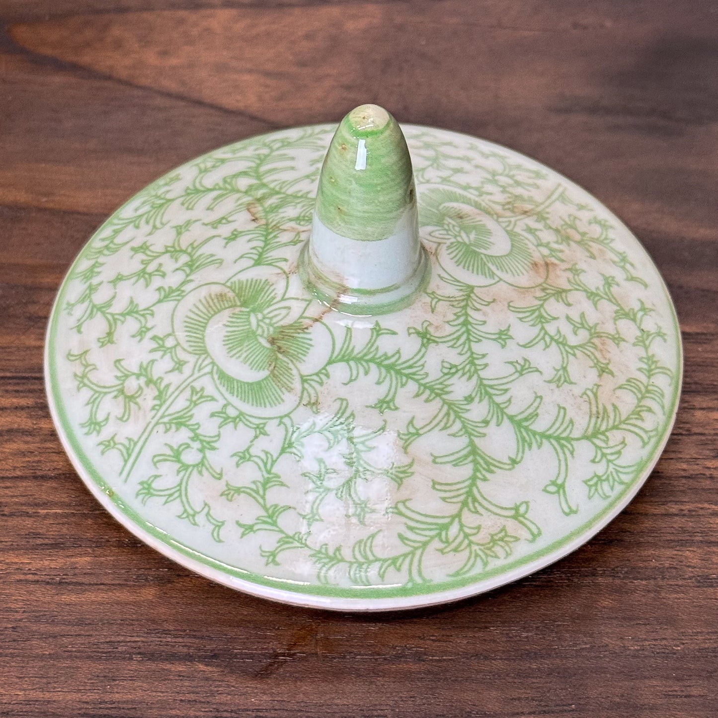 Green ceramic jar with intricate patterns on a wooden surface