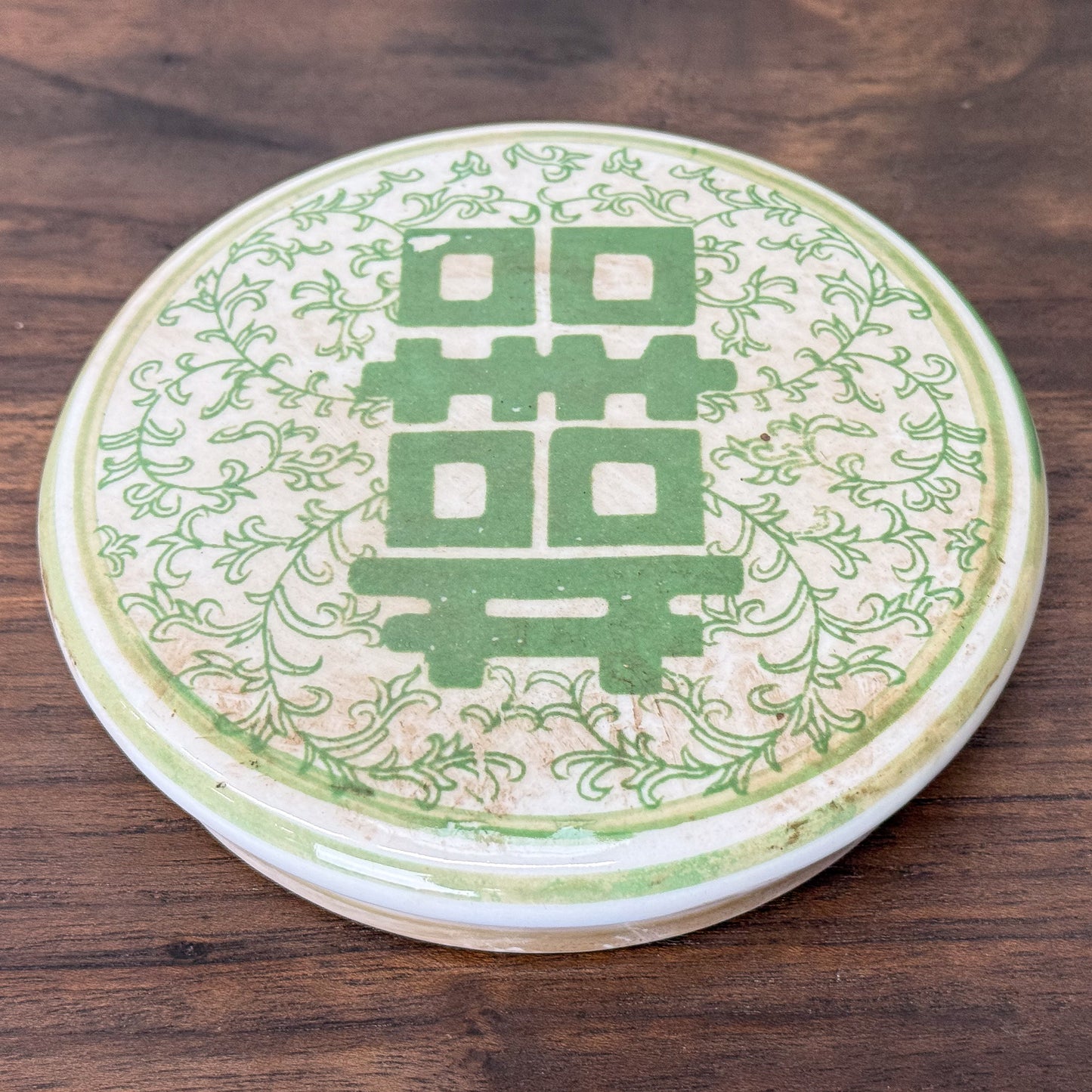 Green and white ceramic jar with floral patterns and a double happiness symbol on a wooden surface.