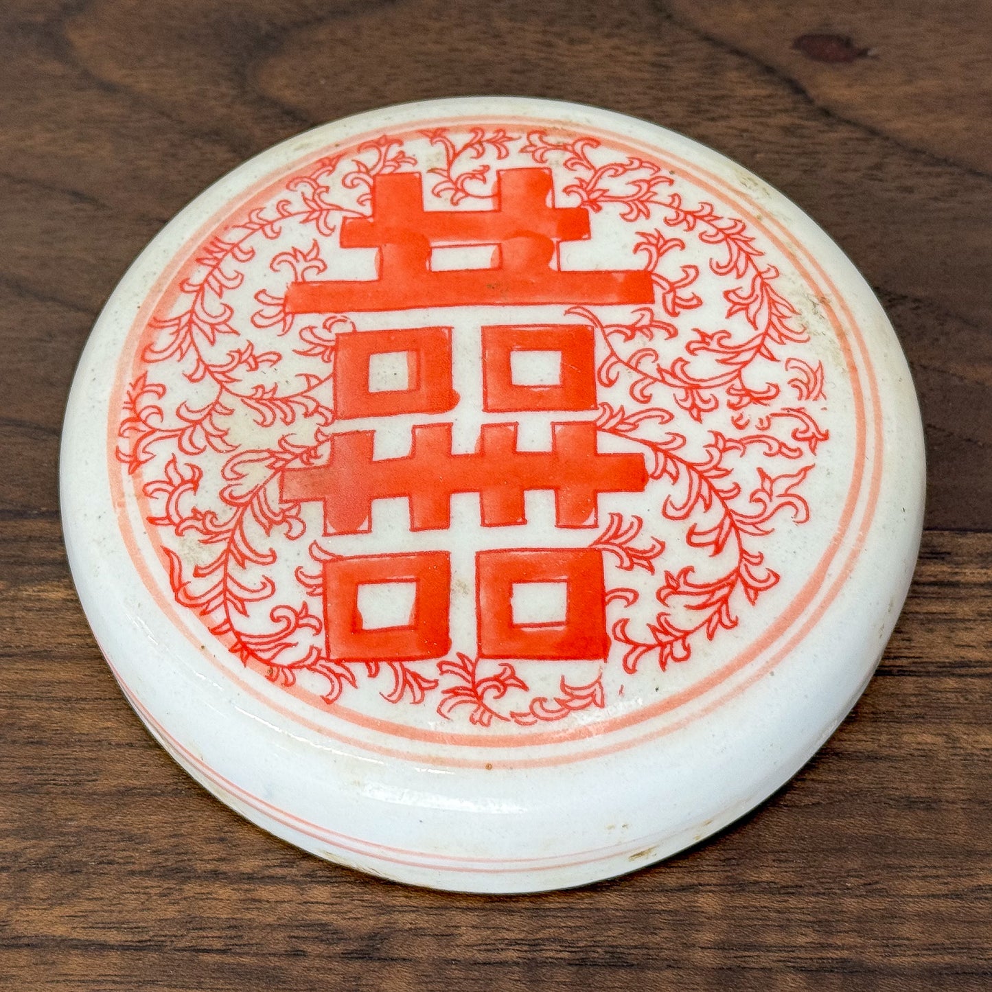 White coaster with red floral design and double happiness symbol on a wooden surface