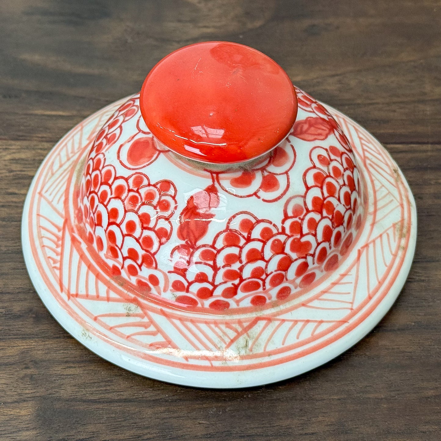 Red and white ceramic jar with phoenix design on a wooden surface.