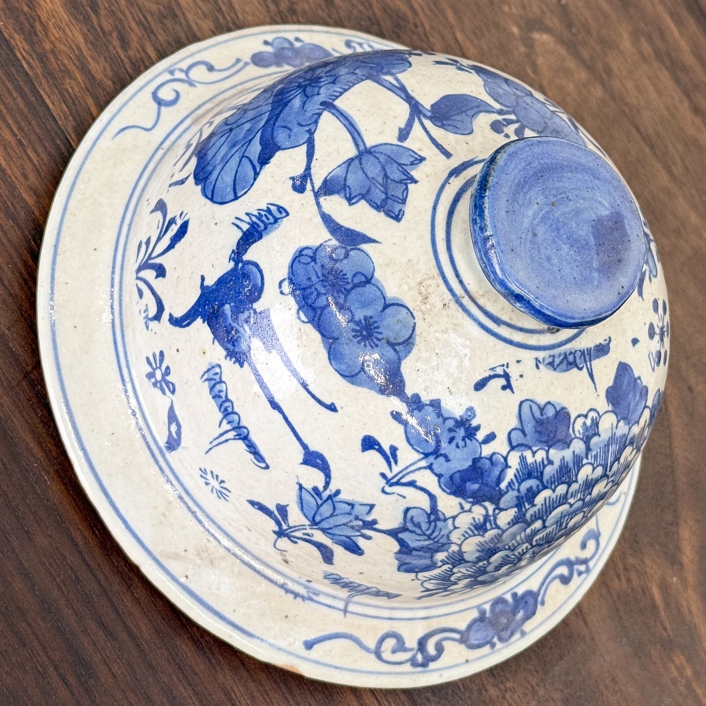 Blue and white ceramic lid with floral and bird design on a wooden surface