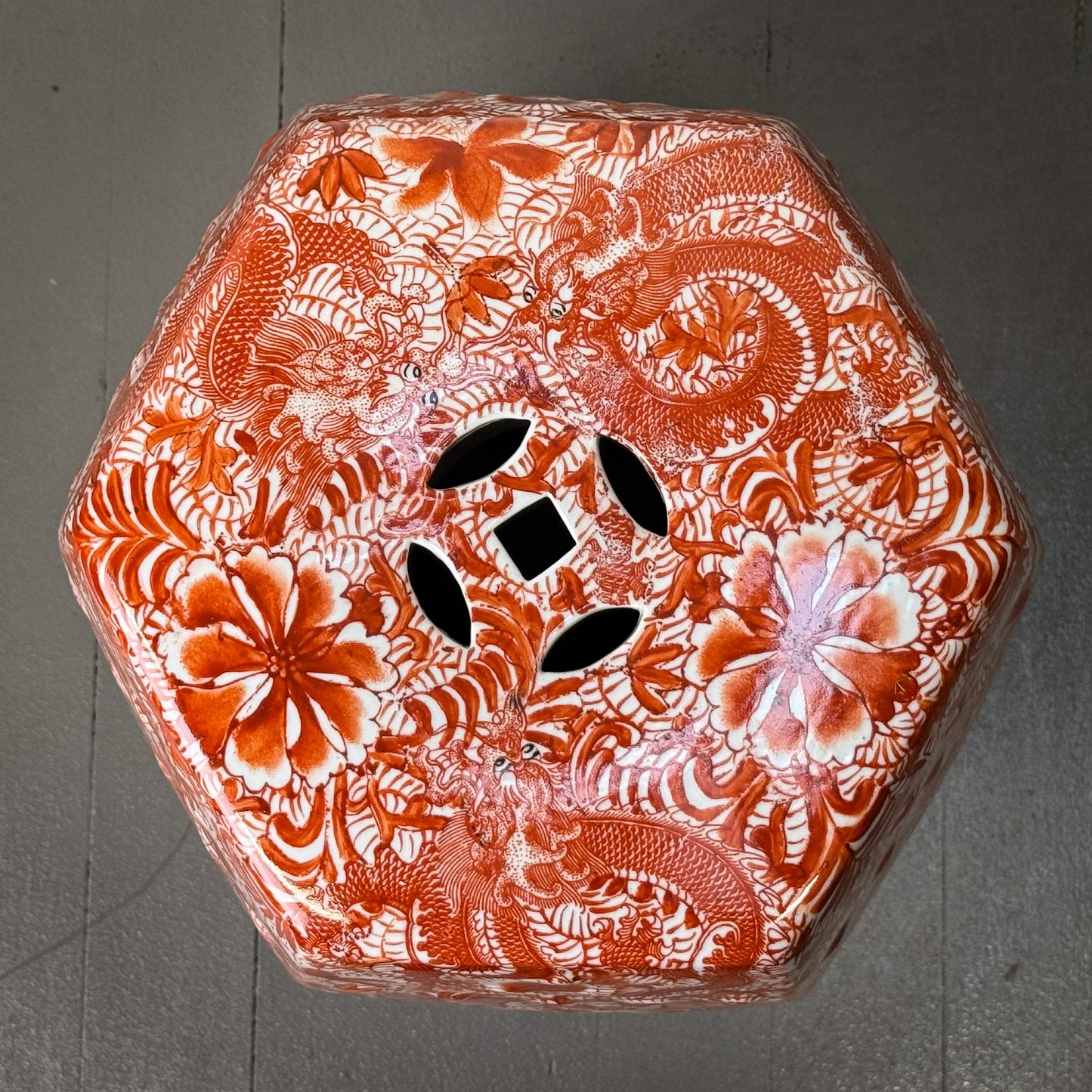Decorative hexagonal stool with intricate red and white floral and dragon design on a gray background