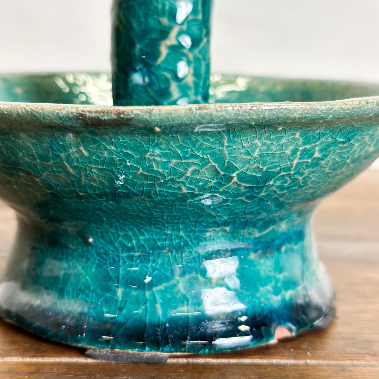 A ceramic candle stand with a crackled turquoise finish and a classical shape with a loop handle on top.