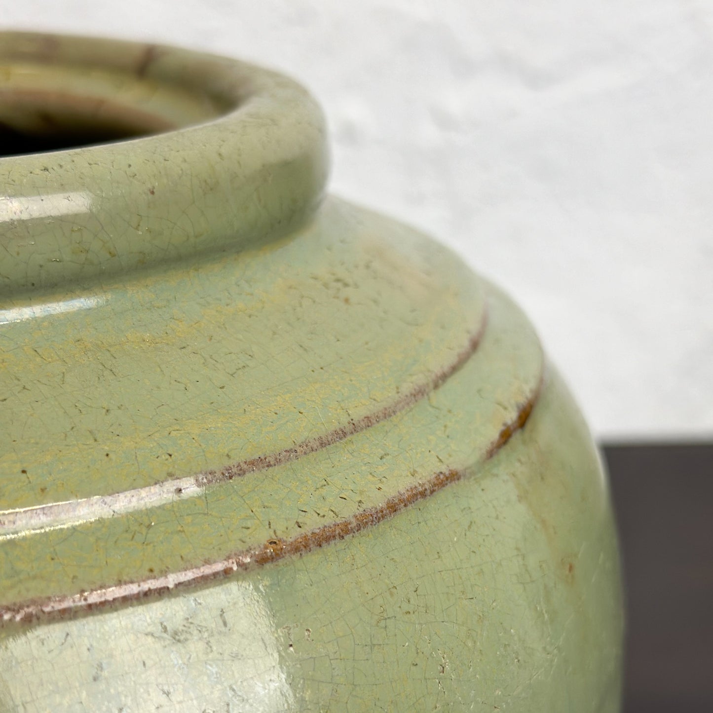 A squat Chinese stoneware pot with a celadon green glaze and a double ridge shoulder.