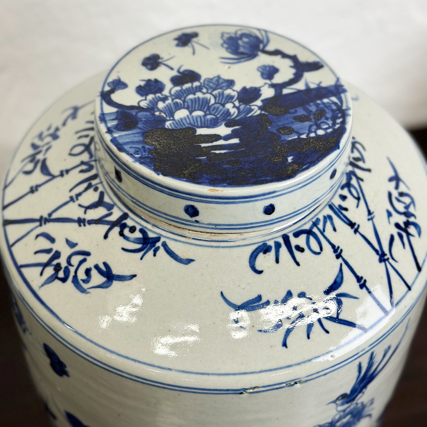 A cylindrical porcelain jar with lid featuring hand-painted designs of flowers and the legendary phoenix bird in blue and white colors.