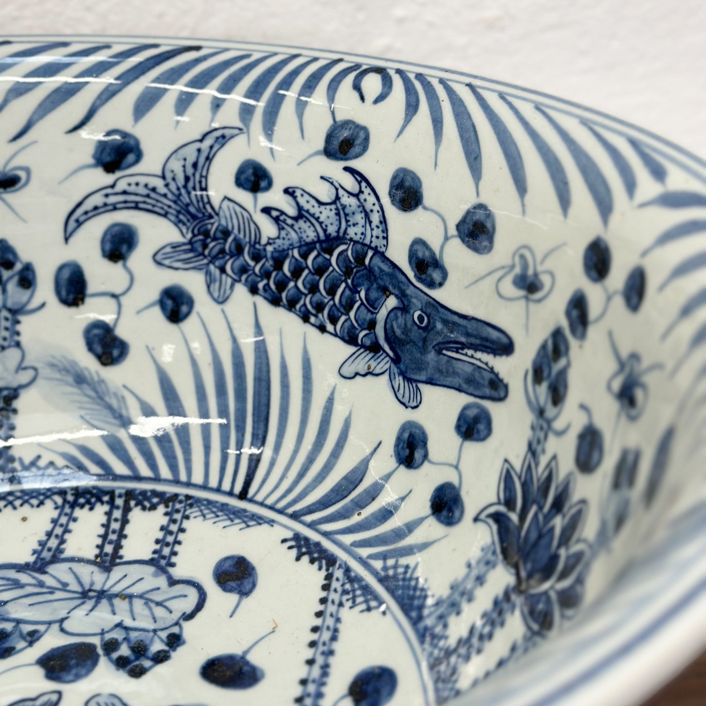 A large porcelain bowl with blue floral and fish patterns on a white background, displayed on a wooden surface.