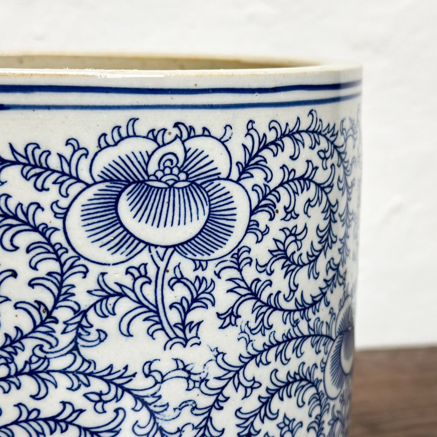 A porcelain paintbrush holder with blue floral patterns on a white background, placed on a wooden surface.