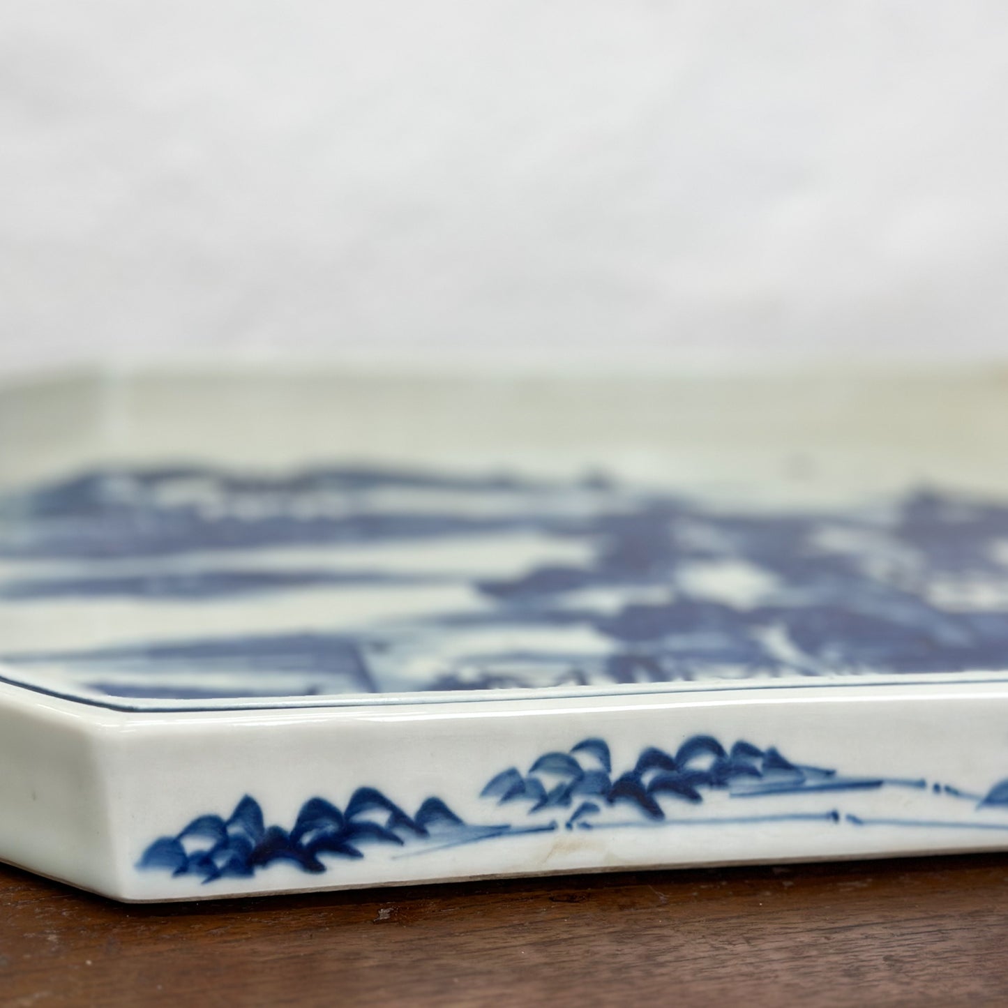 A rectangular porcelain tray with a blue village scene pattern, displayed on a wooden surface.