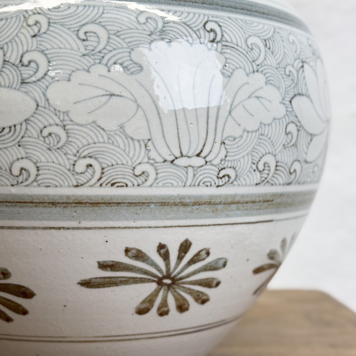 A porcelain vase with a floral pattern, predominantly in shades of green and beige, placed on a wooden surface against a plain wall.