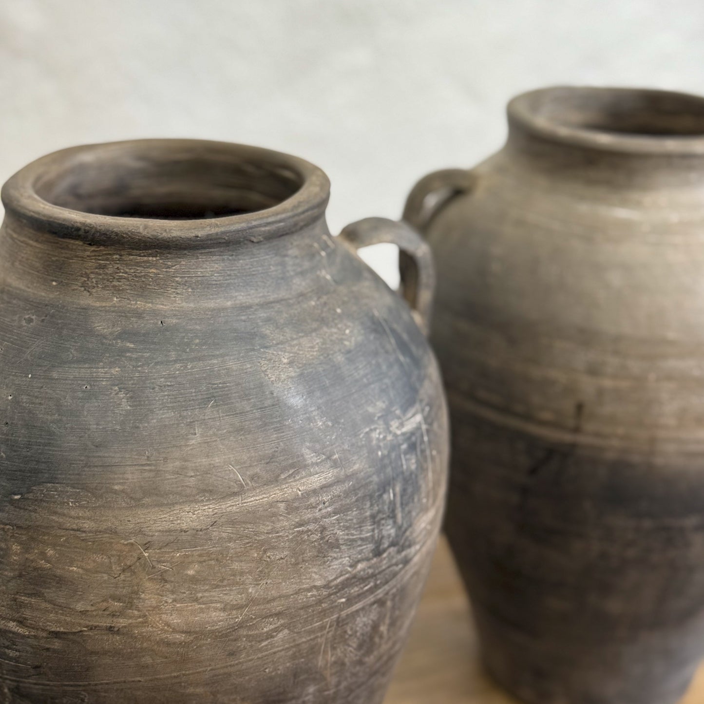 A dark-colored, earthenware vase with a rustic finish, featuring two handles on the side.