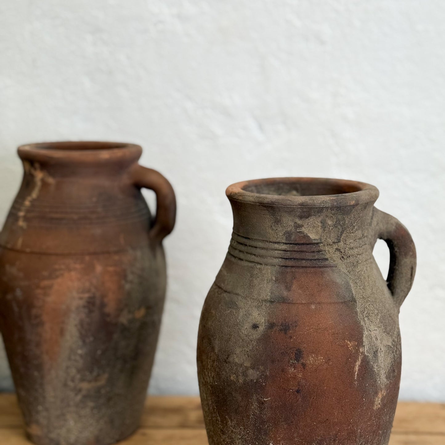 Two rustic clay pots with handles on a wooden surface and light gray background