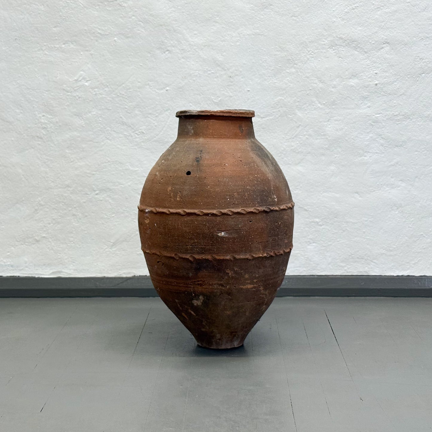 Large brown ceramic jar on a gray floor with a light gray textured wall background