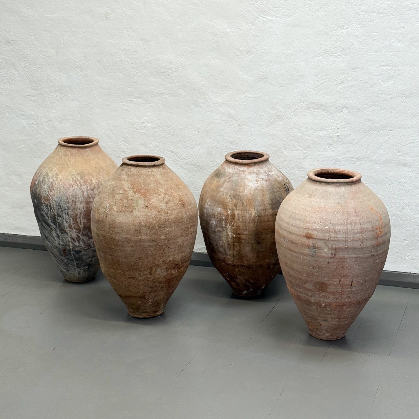 Four large ceramic pots with a textured surface on a gray floor against a light gray wall.