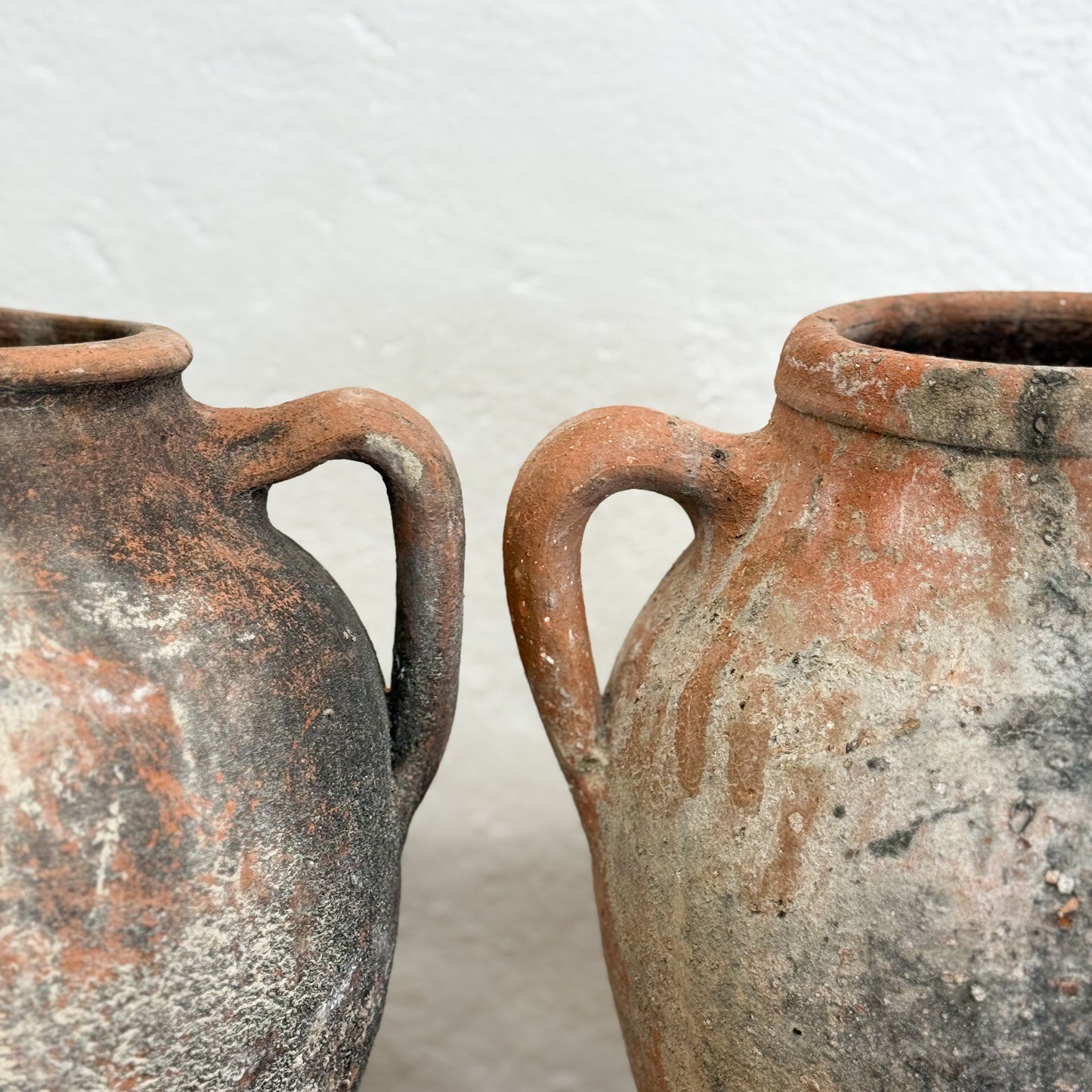 Two rustic clay pots with handles on a light background