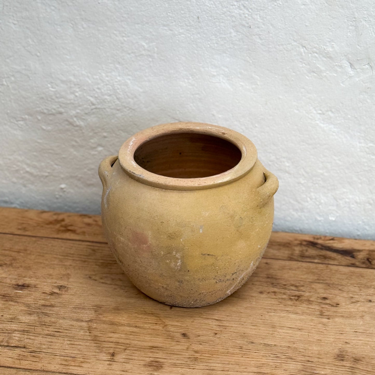 Terracotta pot on a wooden surface with a white textured wall background