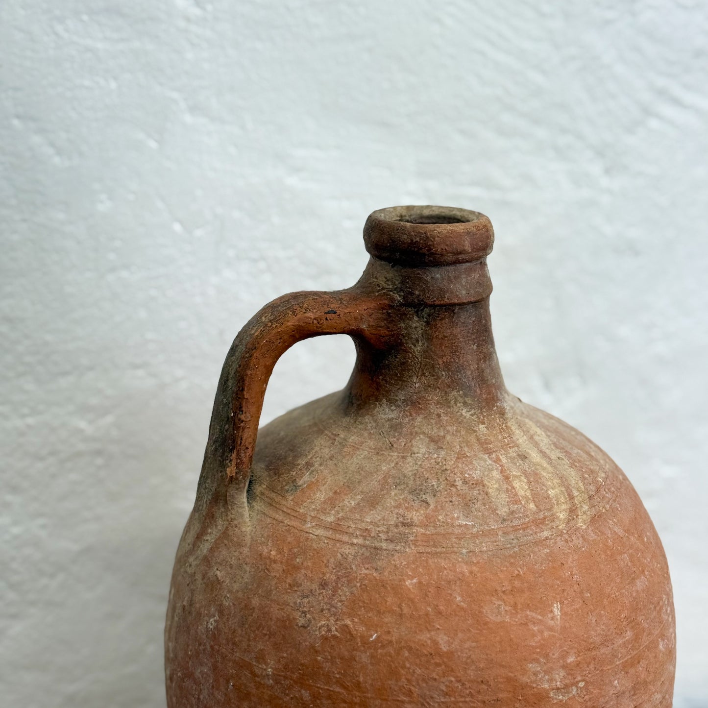 Vintage terracotta jar with a handle on a textured white background