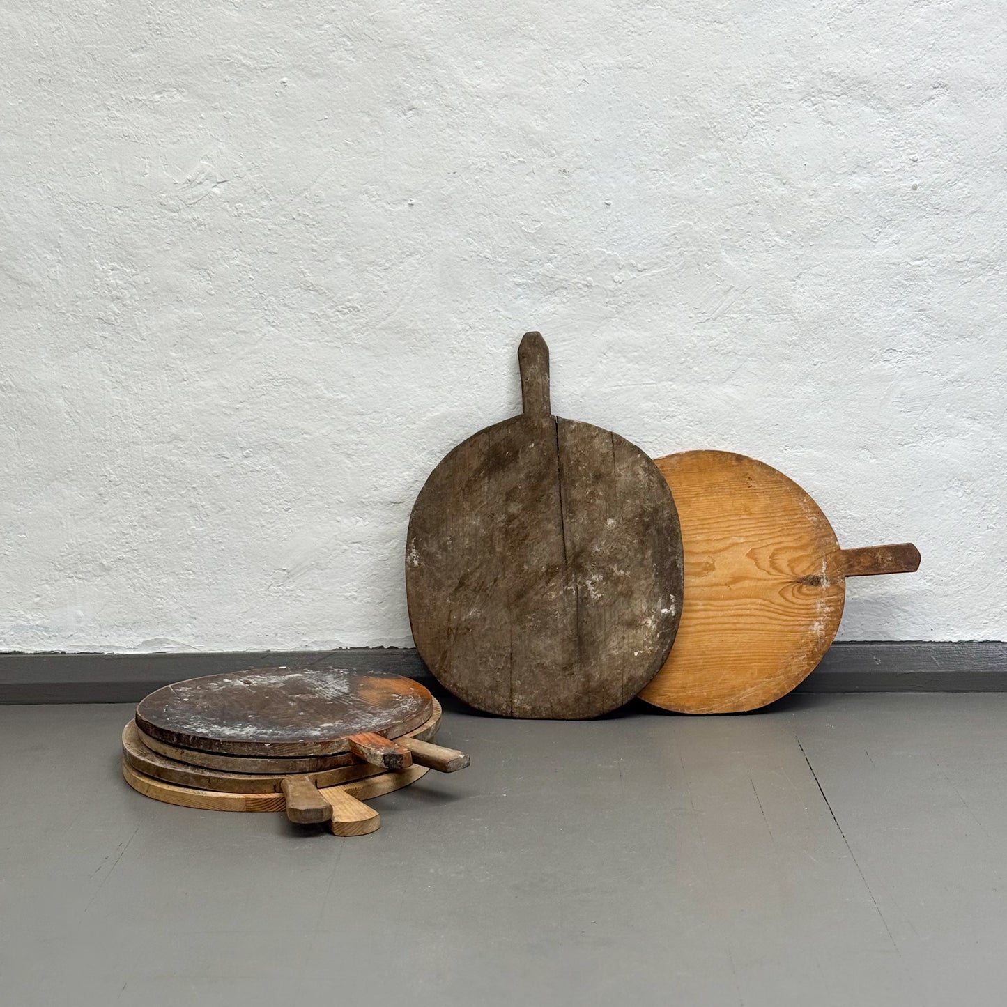 Set of wooden pizza peel tools against a textured white wall.