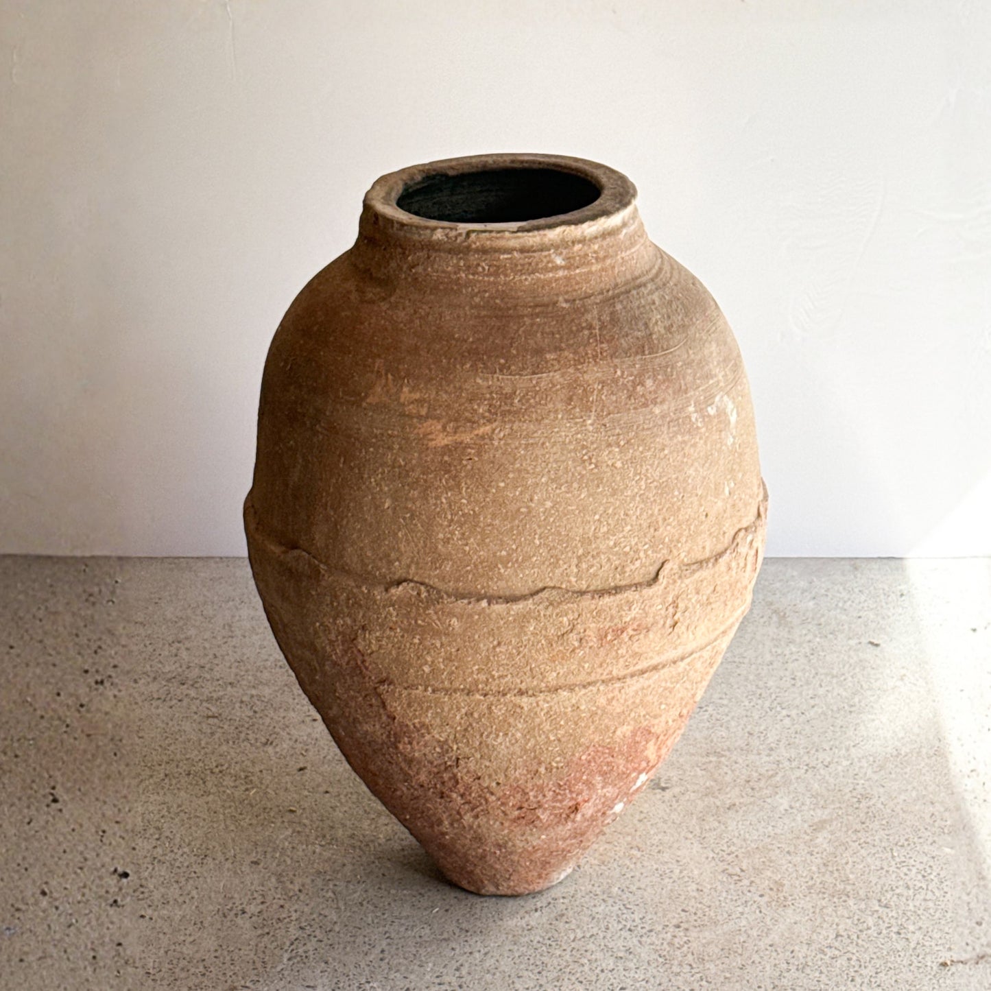 Large terracotta pot on a concrete floor with a white wall background