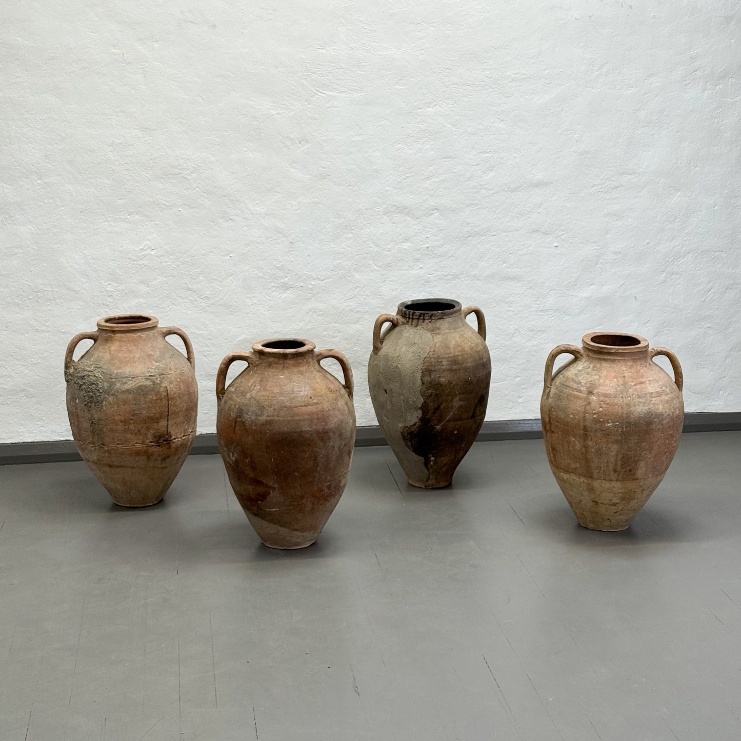 Four rustic clay pots of varying sizes against a textured white wall.