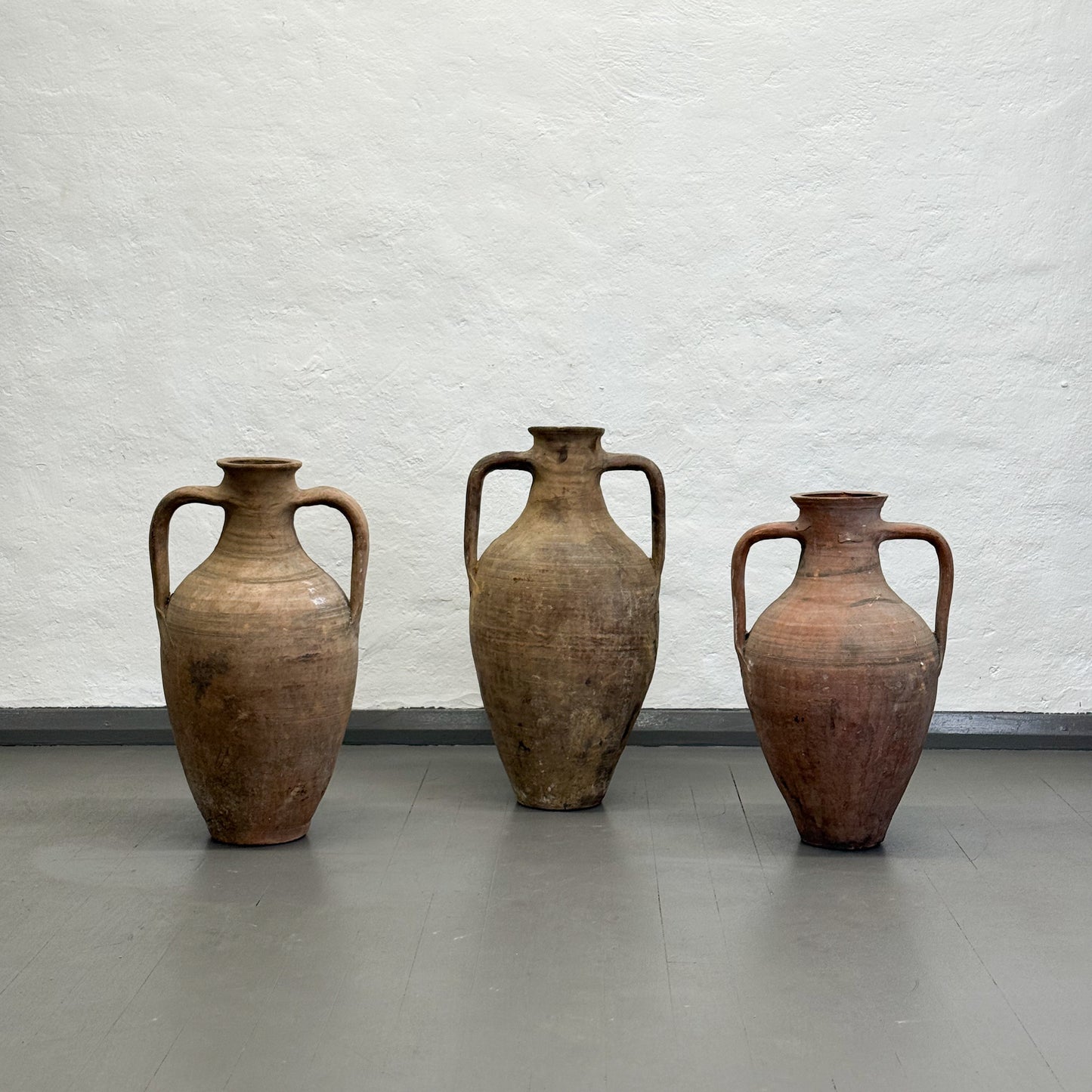 Three large brown ceramic vases against a textured white wall.