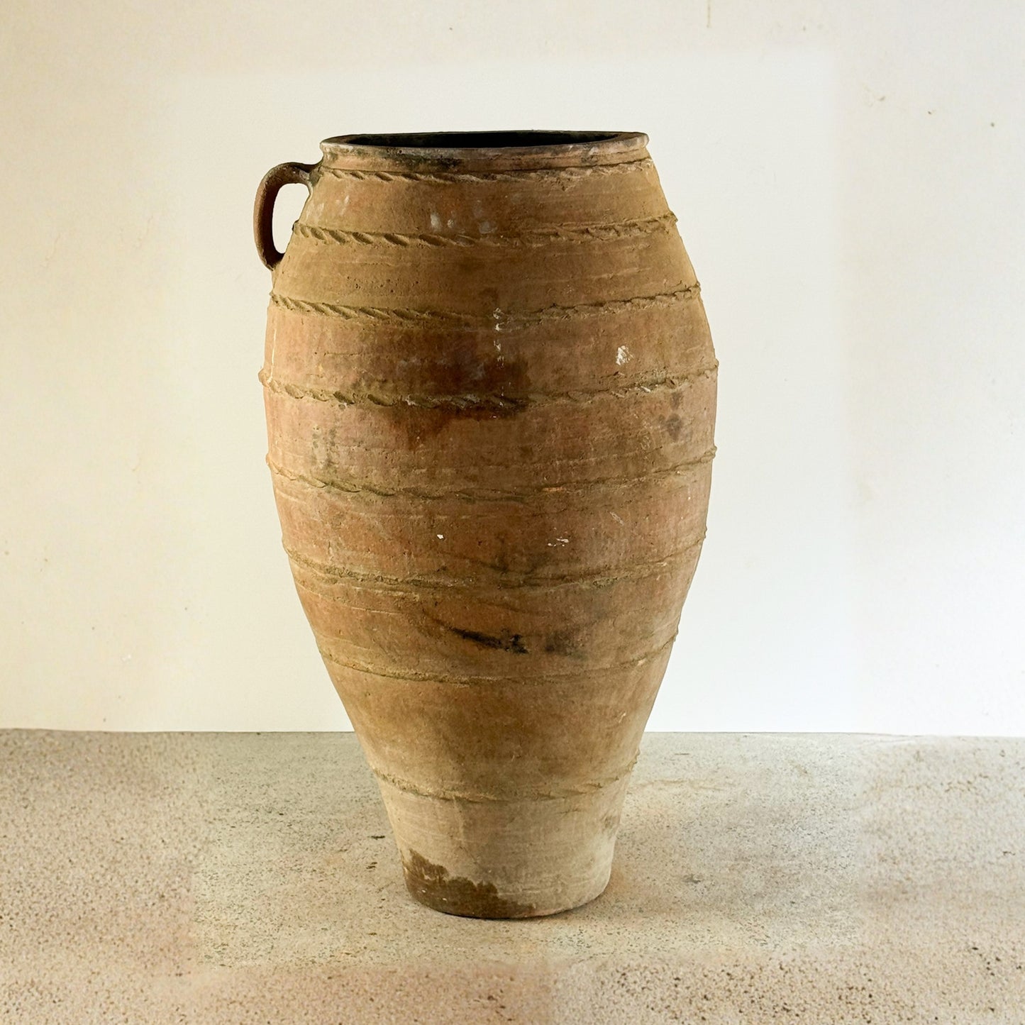 Large terracotta vase on a beige surface with a plain background