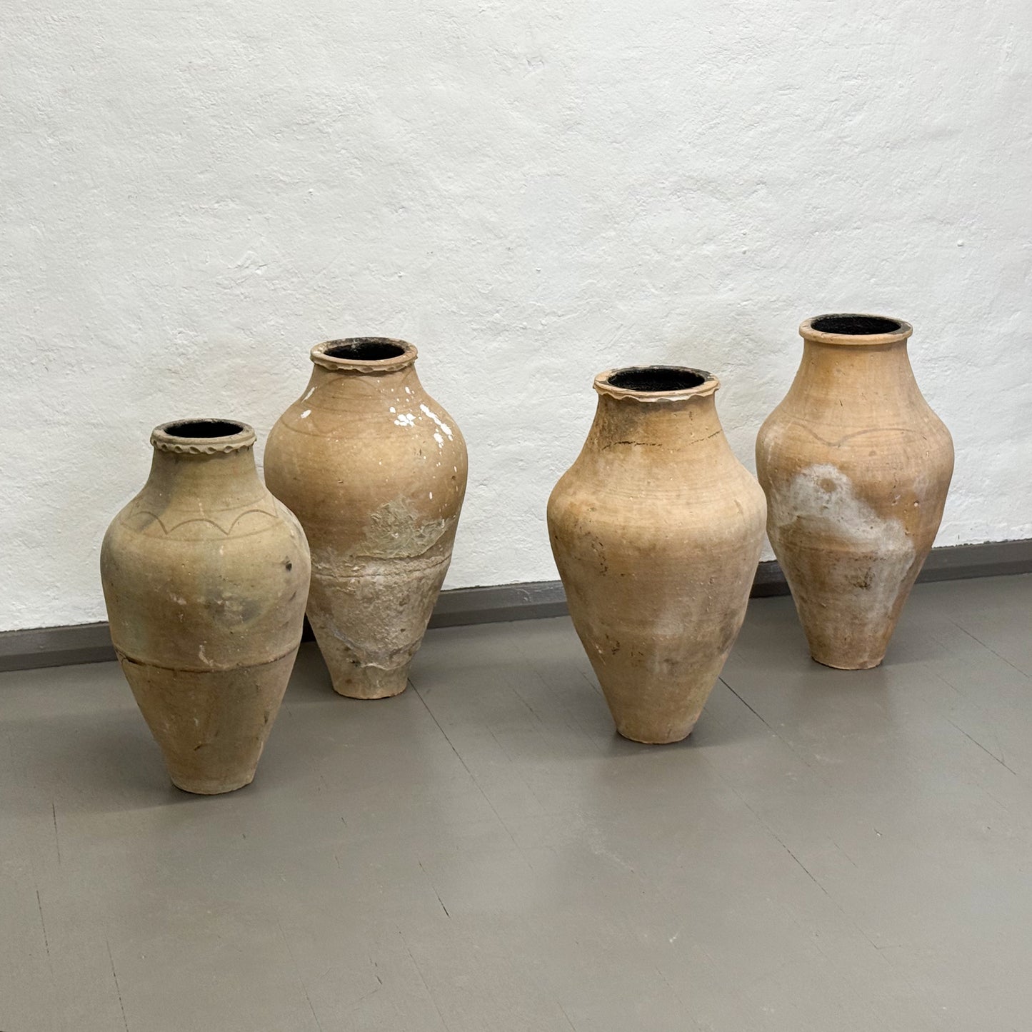 Four large beige ceramic vases against a light gray textured wall.
