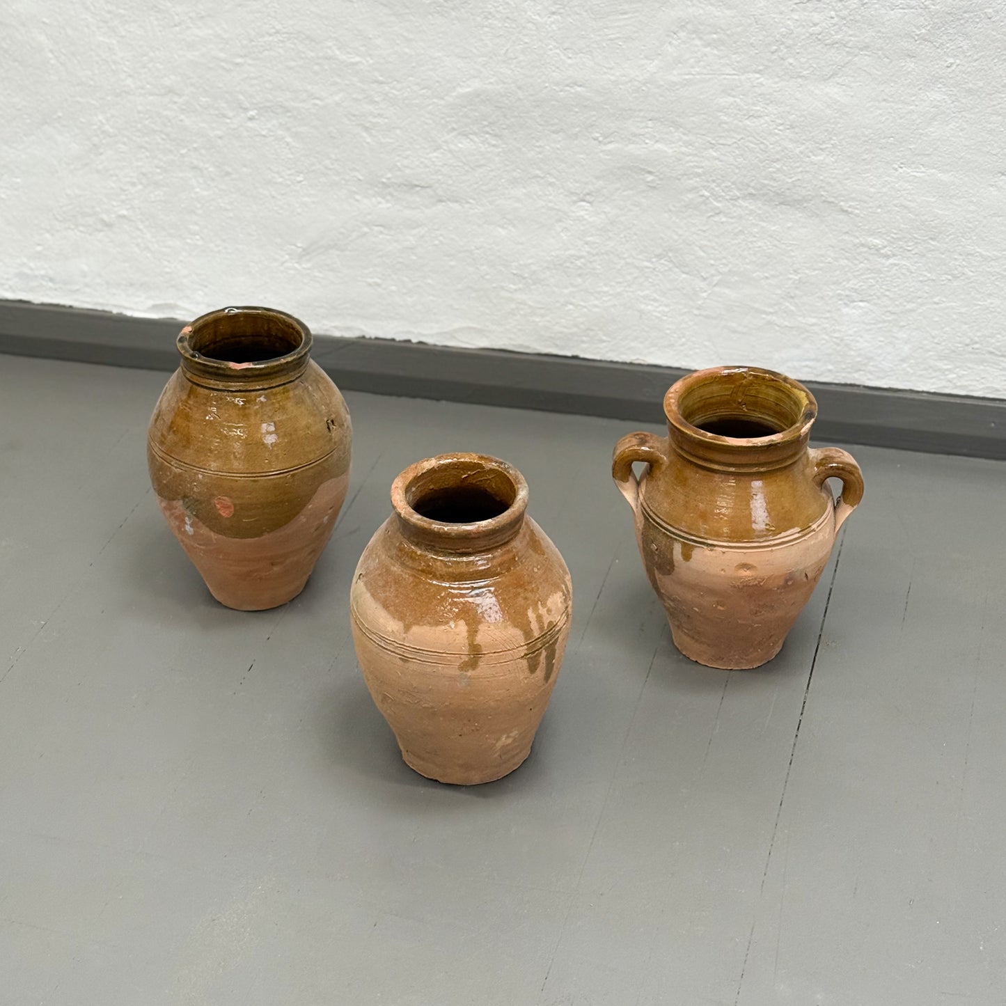 Three brown ceramic pots on a gray floor with a white textured wall background